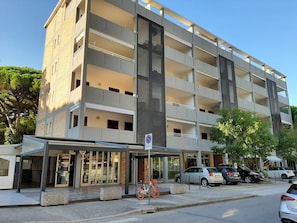 A multi-story hotel with a covered entrance, a bicycle parked outside, and several cars parked on the street. - Flat With Parking Near the Beach (Lignano Sabbiadoro)