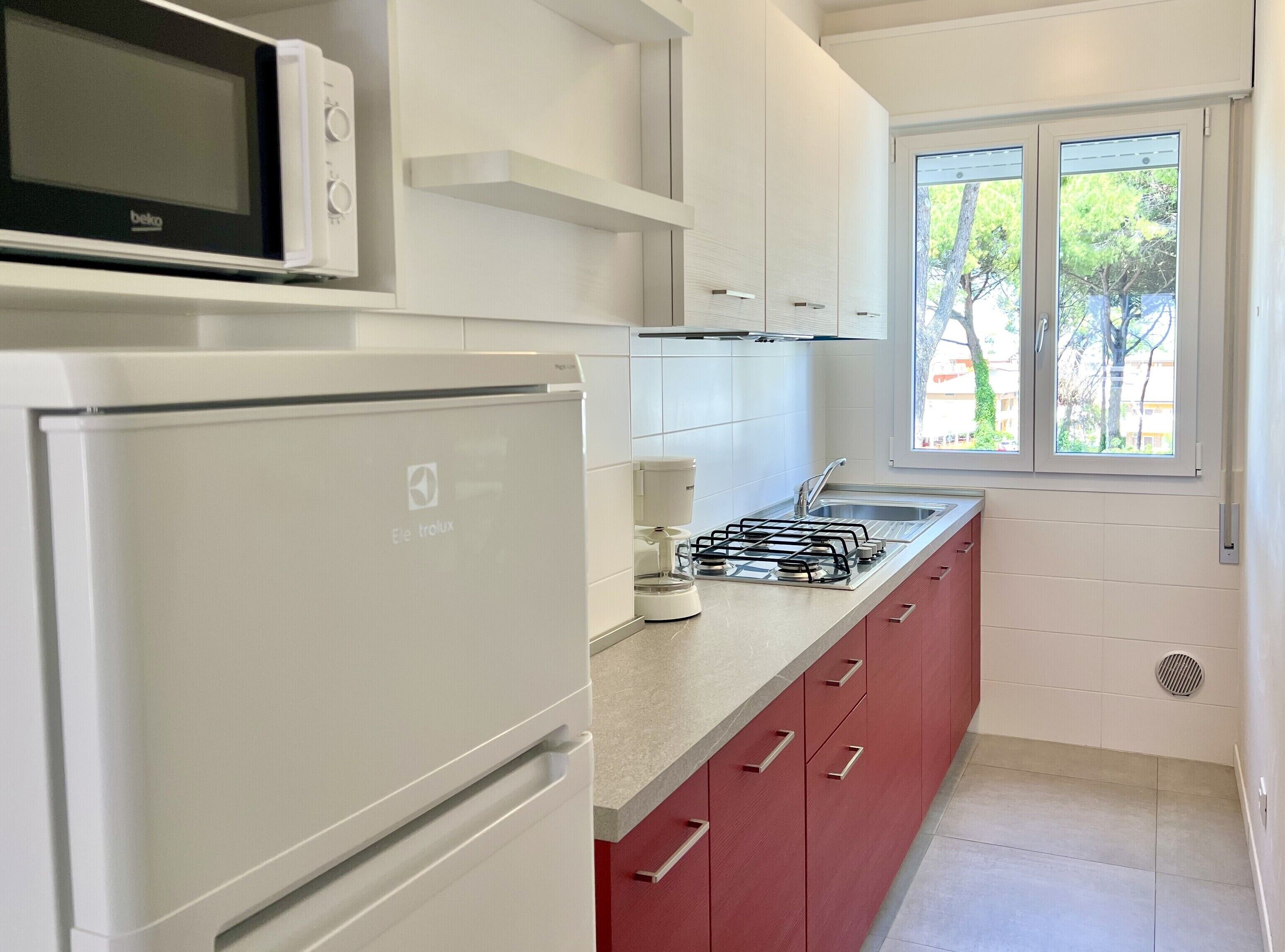 A modern kitchen with a refrigerator, microwave, gas stove, and red cabinets.