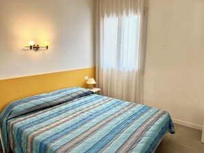 A hotel room with a bed, a nightstand, a lamp, and a wall-mounted light fixture. - Flat With Parking Near the Beach (Lignano Sabbiadoro)
