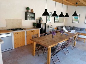 A modern kitchen with wooden cabinets, a dining table, and hanging pendant lights. - Charming Villa in Provence, Poolside Living & Cicada-Filled Evenings (LAURIS)