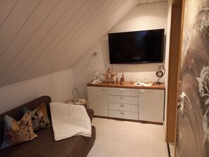 Un dormitorio tipo loft acogedor con techo inclinado, un televisor de pantalla plana, un aparador de madera y un adorno de pared.