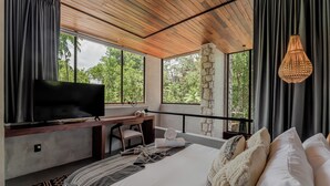 A bedroom with a TV, desk, and bed, large windows, and a hanging light fixture. - Siwa Tulum 2BR Luxury Condo with Private Pool + Rooftop (Tulum)