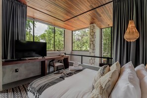 A bedroom with a TV, desk, and bed, large windows, and a hanging light fixture. - Siwa Tulum 2BR Luxury Condo with Private Pool + Rooftop (Tulum)