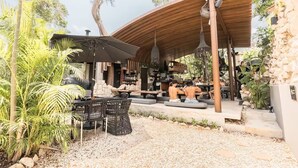 An outdoor seating area with tables and chairs, a covered wooden structure, and a stone wall. - Siwa Tulum 2BR Luxury Condo with Private Pool + Rooftop (Tulum)