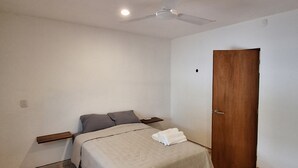 A bedroom with a bed, a ceiling fan, a wooden door, and a small bedside table. - Cozy house 150 meters from the Beach in Chicxulub Puerto (Chicxulub)