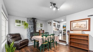 Uma sala de jantar com mesa, cadeiras, lareira e cozinha ao fundo.