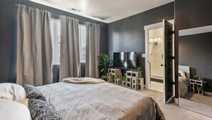 A bedroom with a bed, curtains, a TV, a mirror, and a door leading to a bathroom.