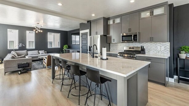 A modern kitchen with grey cabinets, a central island with bar stools, a microwave, and a stove.