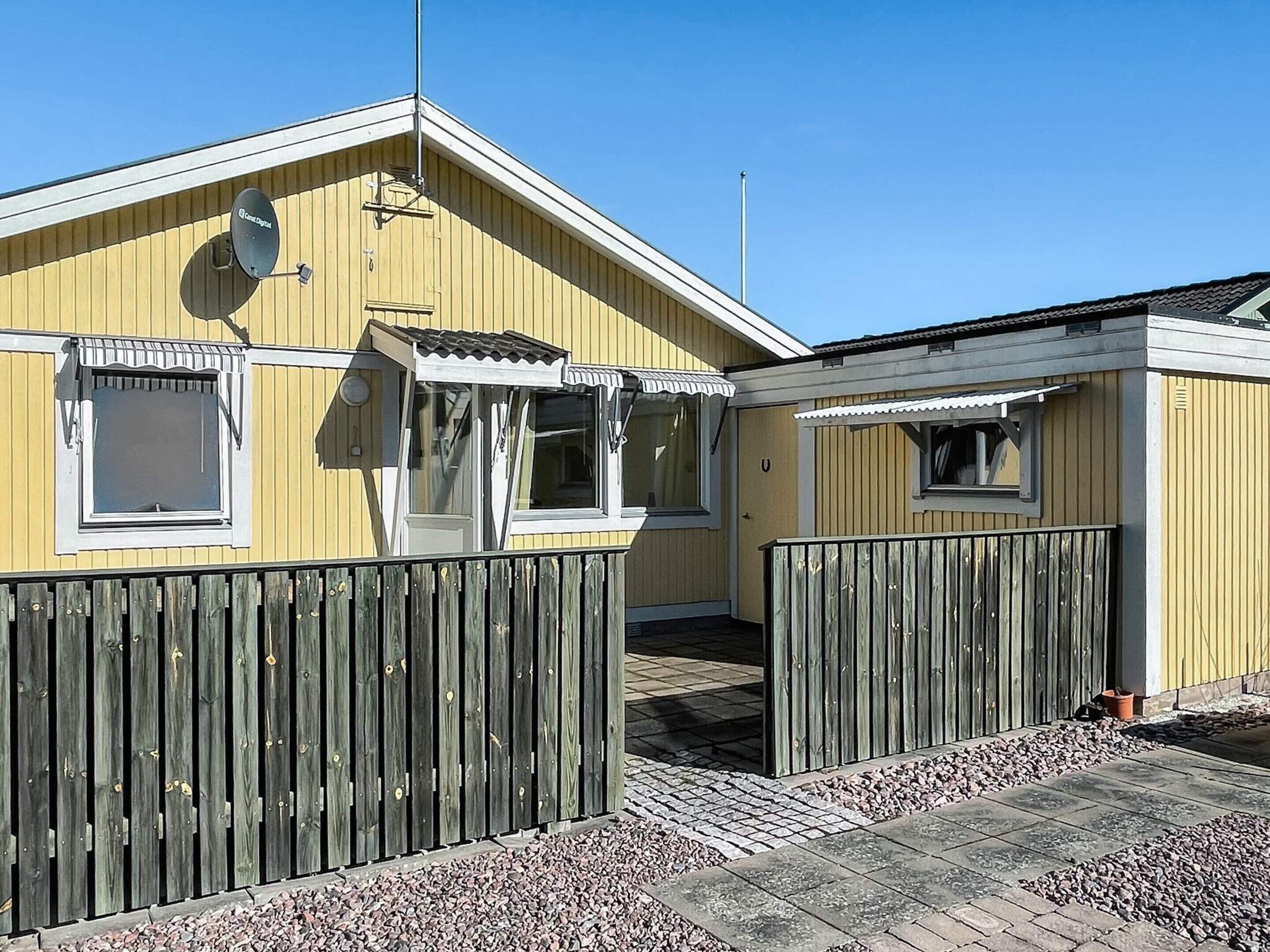 A yellow building with a satellite dish, a wooden fence, and a paved walkway.