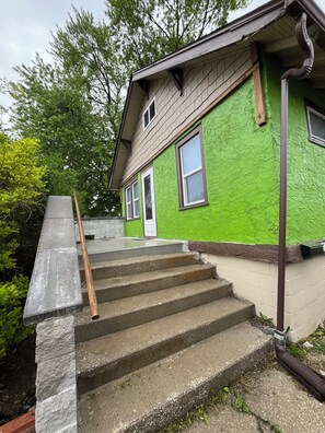 Ein Haus mit grüner Fassade, einer Haustür und einer Treppe aus Beton, die zum Eingang führt.