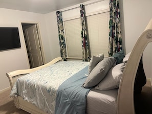 Une chambre à coucher avec un lit, des rideaux, une porte et un téléviseur.