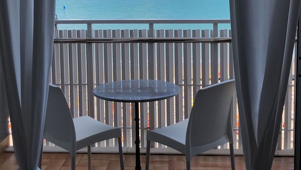 A balcony with a table and chairs, overlooking a body of water. - Seafront Apartment in Lignano (Lignano Sabbiadoro)