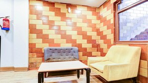 Een hoekzaal met een geaccentueerde bakstenen muur, een brandblusser, een grijze gestoffeerde stoel, een gele fauteuil en een kleine tafel.