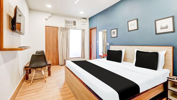 Een hotelkamer met een bed, een bureau, een stoel, een plafondventilator en ingekaderde foto's aan de muur.