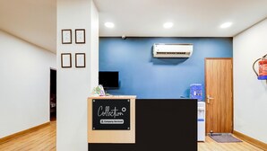 Een receptiegedeelte met een zwarte balie, ingelijste certificaten aan de muur, een airconditioner en een houten deur.