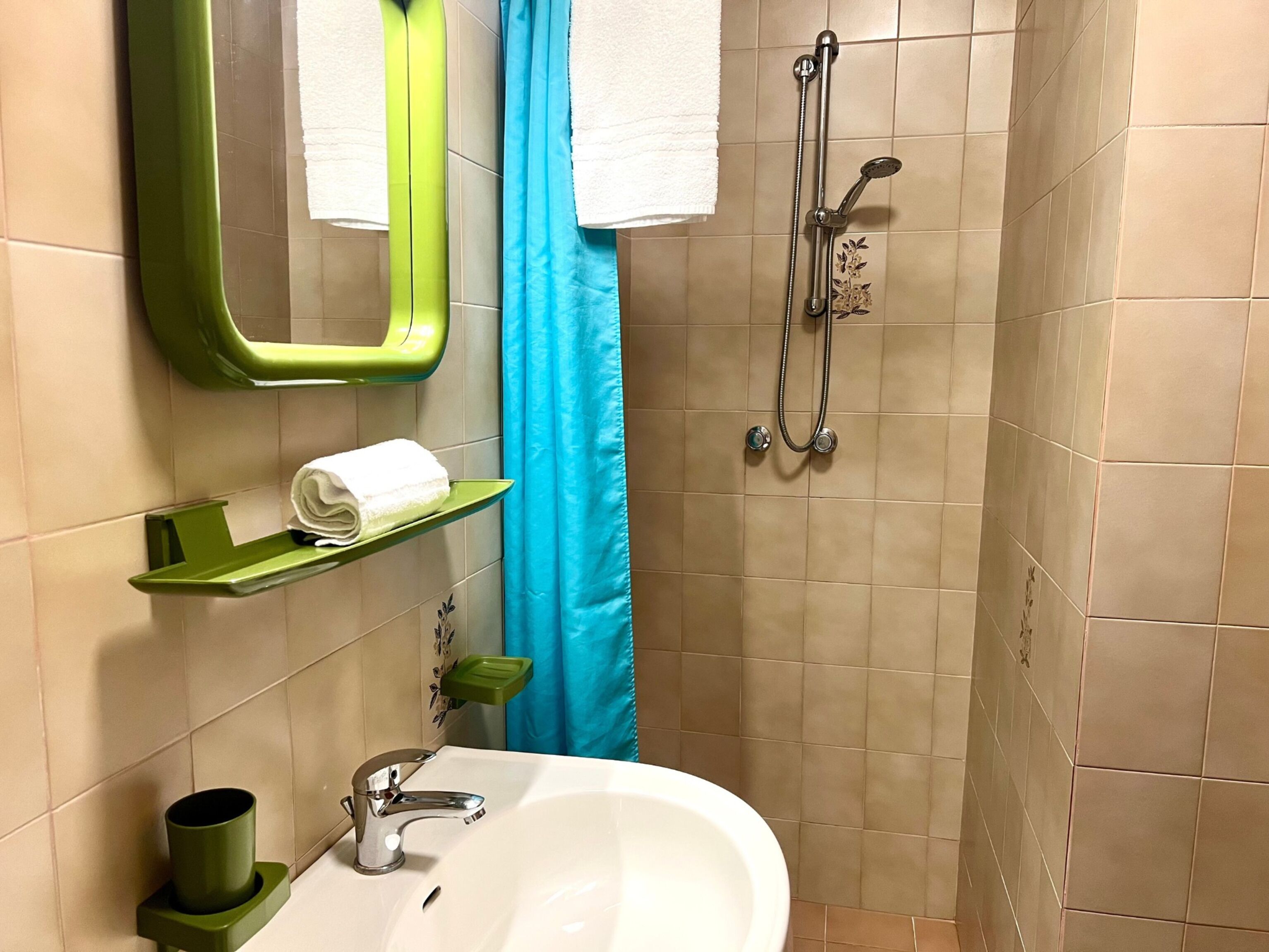 Un baño con lavamanos, espejo, toallero, ducha y estantes verdes.