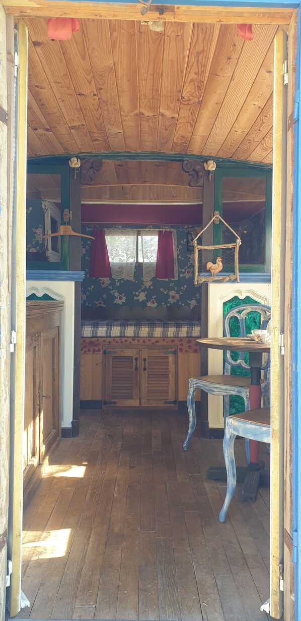 A rustic wooden interior with a wooden floor, a table with a cup, and a hanging birdcage.