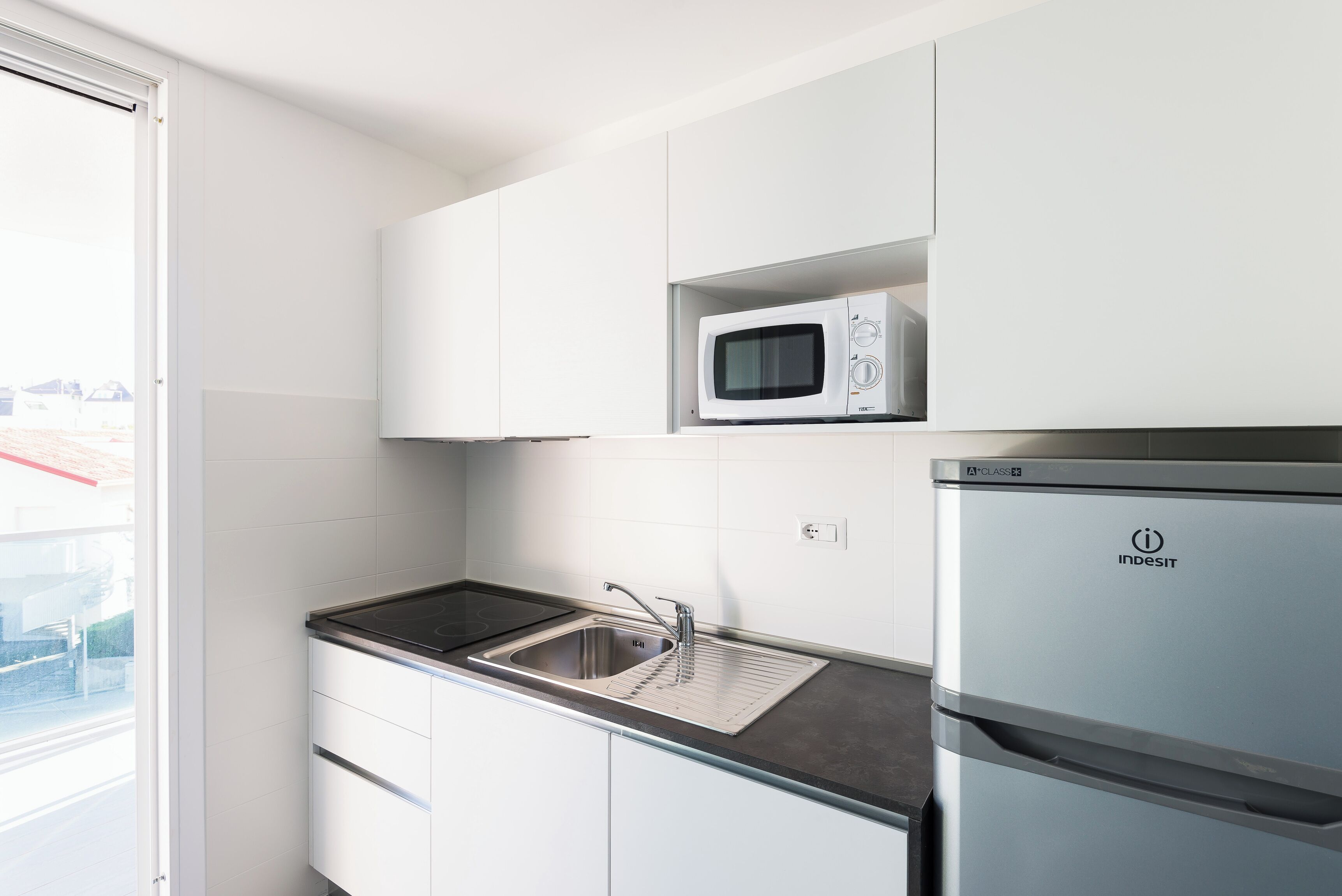 A kitchen with white cabinets, a stainless steel sink, a microwave, and a refrigerator.