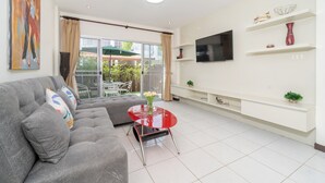 Una sala de estar moderna con un sofá gris, una mesa roja y un televisor montado en la pared.