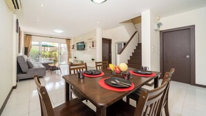 Un comedor con una mesa de madera dispuesta para cuatro personas, un sofá y una escalera que sube a otro nivel.