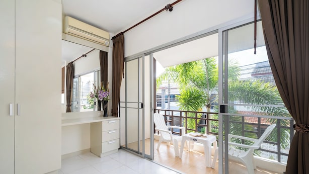 Una habitación moderna con una puerta corrediza de vidrio que da a un balcón con sillas y una mesa blancos.