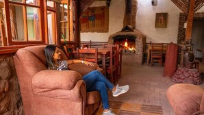 A cozy interior with a stone fireplace, wooden furniture, and a person relaxing on a sofa. - La Casa del Sol Naciente (San Pedro de Atacama)