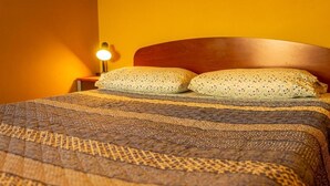 A bed with a patterned blanket, two pillows, and a nightstand with a lamp. - La Casa del Sol Naciente (San Pedro de Atacama)