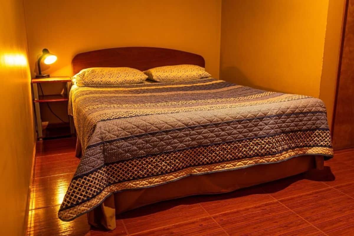 A bed with a patterned quilt, a bedside lamp, and a wooden nightstand.