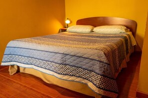 A bed with a patterned bedspread, a wooden headboard, and a bedside lamp. - La Casa del Sol Naciente (San Pedro de Atacama)