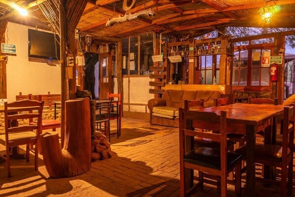 A rustic interior with wooden furniture, a bar area, and a television mounted on the wall. - La Casa del Sol Naciente (San Pedro de Atacama)