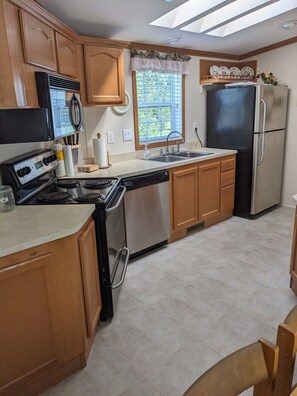 A kitchen with wooden cabinets, a stainless steel refrigerator, a dishwasher, and a window with blinds. - CAMP : 2-bedroom mobile home camp - lake access to Chazy Lake in Ellenburg Depot (Ellenburg Depot)