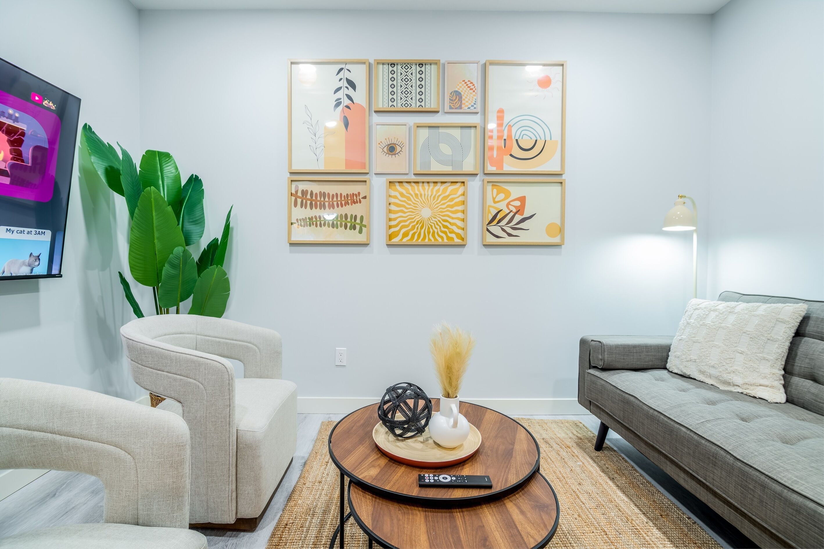 A living room with a sofa, two armchairs, a coffee table, and a TV mounted on the wall.