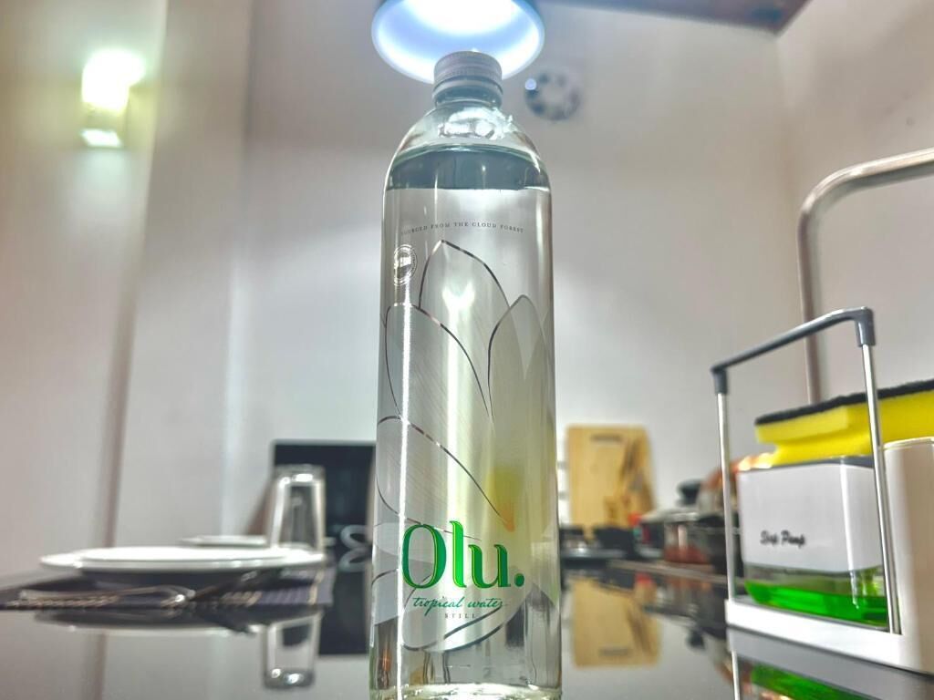 Eine Flasche Oulu-Tropic-Wasser steht auf einem Tisch in einem Raum mit weißer Wand und Deckenlampe.