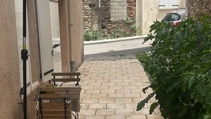 Un patio empedrado con una mesa y sillas bajo un toldo, una pared de ladrillo, y un coche estacionado en la calle.