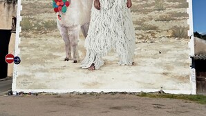 Un mural que muestra a una persona y un llama con vestimenta tradicional, con montañas al fondo.