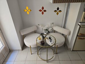 Een hoekzaal met twee witte, beklede stoelen, een ronde tafel met gouden poot en een decoratief paneel aan de muur.