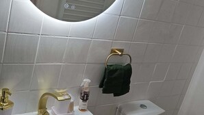 Un baño con un lavamanos blanco, un grifo dorado, un espejo redondo, un inodoro y un perchero para toallas.