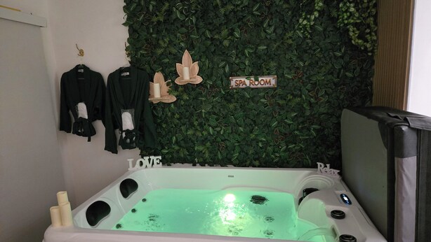 Un cuarto de spa con una pared de hojas verdes, un letrero que dice 'SPA ROOM' y un jacuzzi con chorros de agua.