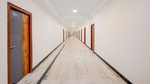 Un long couloir étroit, avec des portes de chaque côté, un sol en marbre et des spots encastrés au plafond.