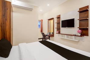 A hotel room with a bed, a desk with a chair, a mounted TV, and built-in shelves.