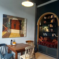 A dining area with a table, chairs, a painting, and a bookshelf.