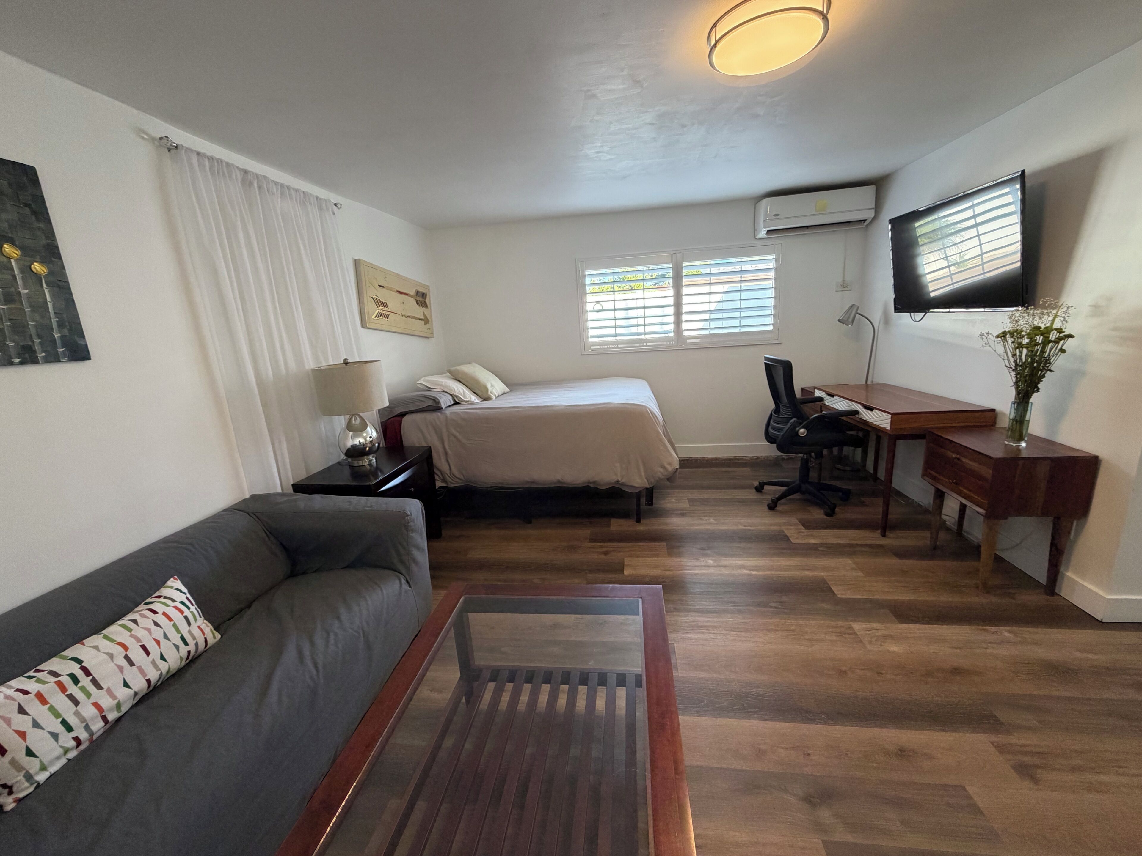 Habitación de hotel pequeña con cama, escritorio, silla, sofá y televisor.