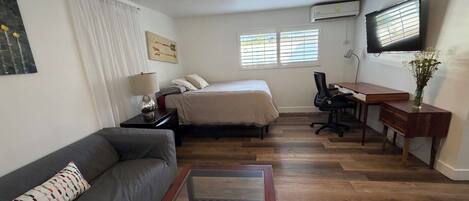 Habitación de hotel pequeña con cama, escritorio, silla, sofá y televisor.