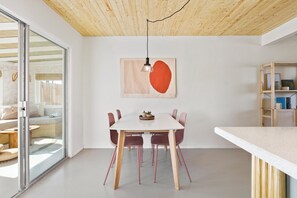 A modern dining area with a white table, red chairs, and a wooden ceiling. - Zen House, serene & close to everything (Yucca Valley)
