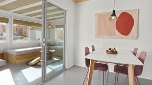 En modern inredning med en glasdörr som leder ut till en uteplats, ett vitt matbord med stolar och ett träpanelat tak.