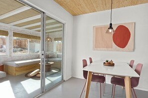 A modern interior with a glass door leading to a patio, a white dining table with chairs, and a wooden ceiling. - Zen House, serene & close to everything (Yucca Valley)