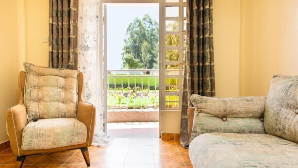 A room with a sofa, a chair, a view through a door to a balcony, and a patterned rug. - Ashville Homes (Meru)
