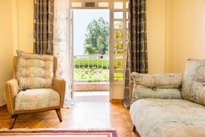 Quarto com sofá, uma cadeira, vista para uma varanda através de uma porta e um tapete estampado.