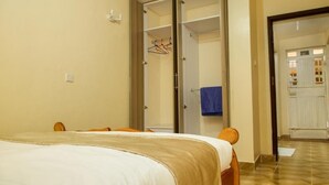 A bedroom with a bed, a wardrobe, and a bathroom visible through an open door. - Ashville Homes (Meru)