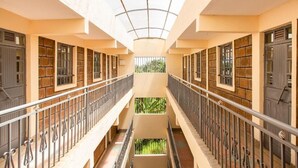A multi-level corridor with a central open space, railings, and doors on both sides. - Ashville Homes (Meru)